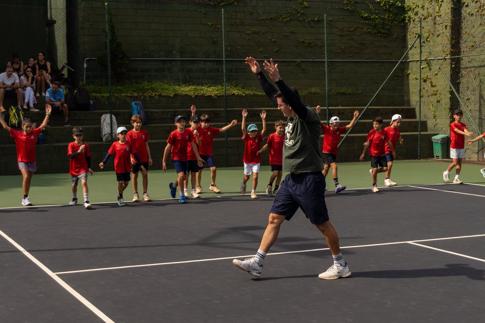 Turma de crianças em aula de tênis na Heart Tennis Academy, camisas vermelhas na quadra